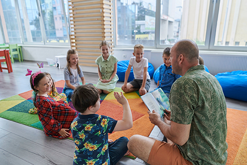 Lehrperson sitzt mit Kindern im Kreis und liest vor.