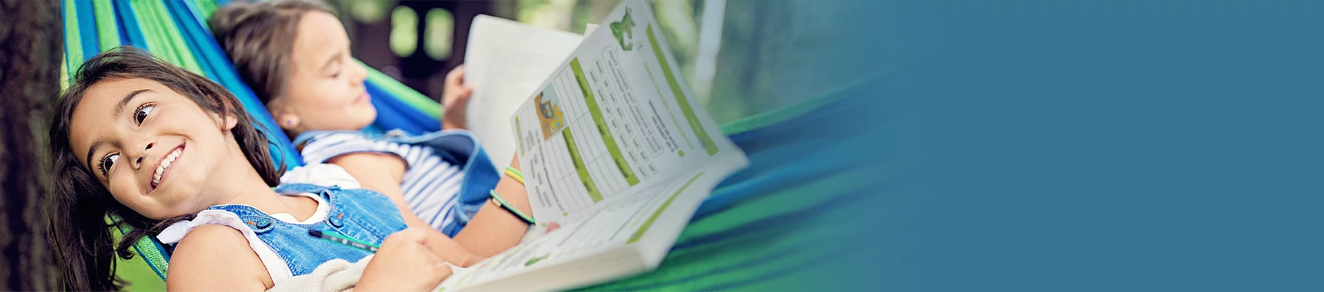 2 Kinder liegen in einer Hängematte und lesen in einem Karibu-Ferienheft